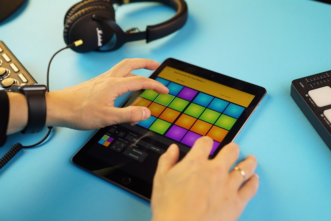 Hands using a tablet with a music app on a blue table.